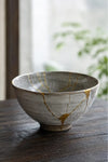 A close-up of a Kintsugi repaired bowl showing beautiful gold lines against dark ceramic.